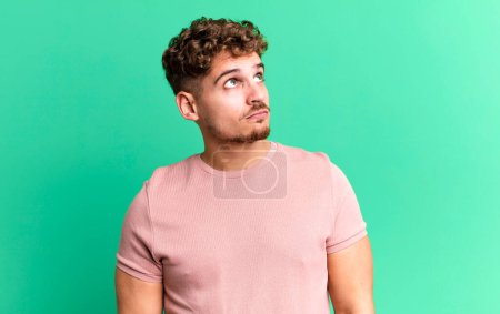 Photo for Young adult caucasian man with a worried, confused, clueless expression, looking up to copy space, doubting - Royalty Free Image