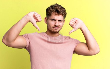 Photo for Young adult caucasian man looking sad, disappointed or angry, showing thumbs down in disagreement, feeling frustrated - Royalty Free Image