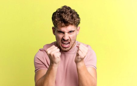 Photo for Young adult caucasian man shouting aggressively with annoyed, frustrated, angry look and tight fists, feeling furious - Royalty Free Image