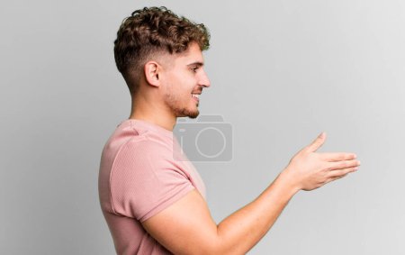 Photo for Young adult caucasian man smiling, greeting you and offering a hand shake to close a successful deal, cooperation concept - Royalty Free Image