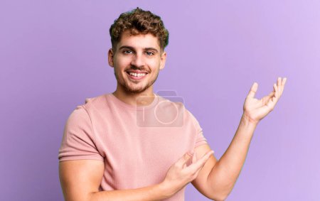 Téléchargez les photos : Young adult caucasian man smiling proudly and confidently, feeling happy and satisfied and showing a concept on copy space - en image libre de droit