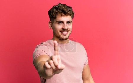 Téléchargez les photos : Young adult caucasian man smiling proudly and confidently making number one pose triumphantly, feeling like a leader - en image libre de droit