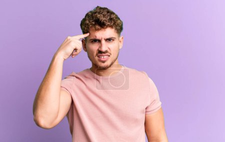 Photo for Young adult caucasian man feeling confused and puzzled, showing you are insane, crazy or out of your mind - Royalty Free Image