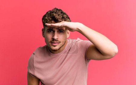Photo for Young adult caucasian man looking bewildered and astonished, with hand over forehead looking far away, watching or searching - Royalty Free Image