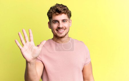 Photo for Young adult caucasian man smiling and looking friendly, showing number five or fifth with hand forward, counting down - Royalty Free Image