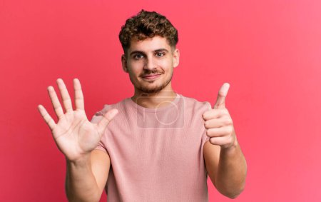 Photo for Young adult caucasian man smiling and looking friendly, showing number six or sixth with hand forward, counting down - Royalty Free Image