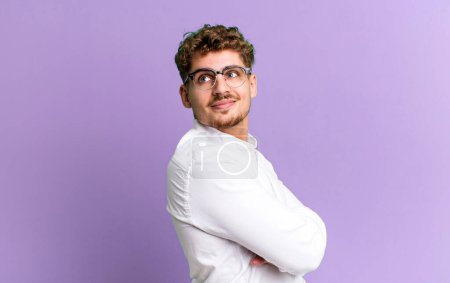 Foto de Young adult caucasian man smiling gleefully, feeling happy, satisfied and relaxed, with crossed arms and looking to the side - Imagen libre de derechos
