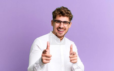 Foto de Young adult caucasian man feeling happy, cool, satisfied, relaxed and successful, pointing at camera, choosing you - Imagen libre de derechos