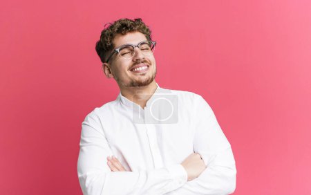 Photo for Young adult caucasian man laughing happily with arms crossed, with a relaxed, positive and satisfied pose - Royalty Free Image