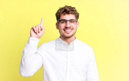 Photo for Young adult caucasian man smiling cheerfully and happily, pointing upwards with one hand to copy space - Royalty Free Image