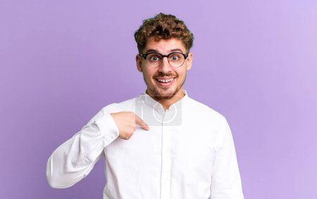 Téléchargez les photos : Young adult caucasian man looking happy, proud and surprised, cheerfully pointing to self, feeling confident and lofty - en image libre de droit