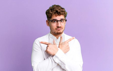 Photo for Young adult caucasian man looking puzzled and confused, insecure and pointing in opposite directions with doubts - Royalty Free Image