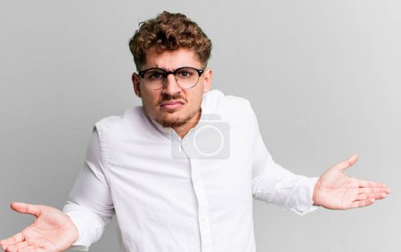 Téléchargez les photos : Young adult caucasian man feeling clueless and confused, having no idea, absolutely puzzled with a dumb or foolish look - en image libre de droit
