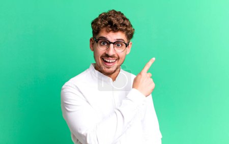 Téléchargez les photos : Young adult caucasian man looking excited and surprised pointing to the side and upwards to copy space - en image libre de droit