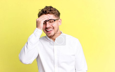 Téléchargez les photos : Young adult caucasian man laughing and slapping forehead like saying doh! I forgot or that was a stupid mistake - en image libre de droit