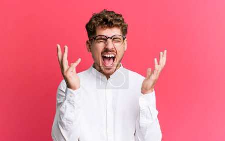 Photo for Young adult caucasian man furiously screaming, feeling stressed and annoyed with hands up in the air saying why me - Royalty Free Image