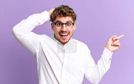 Foto de Young adult caucasian man laughing, looking happy, positive and surprised, realizing a great idea pointing to lateral copy space - Imagen libre de derechos