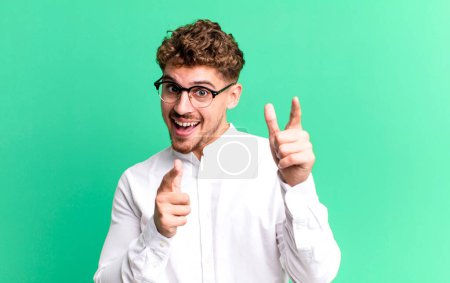 Foto de Young adult caucasian man smiling with a positive, successful, happy attitude pointing to the camera, making gun sign with hands - Imagen libre de derechos