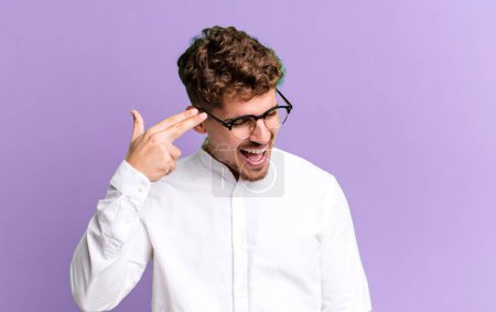 Foto de Young adult caucasian man looking unhappy and stressed, suicide gesture making gun sign with hand, pointing to head - Imagen libre de derechos