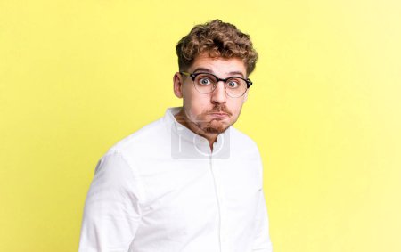 Photo for Young adult caucasian man with a goofy, crazy, surprised expression, puffing cheeks, feeling stuffed, fat and full of food - Royalty Free Image