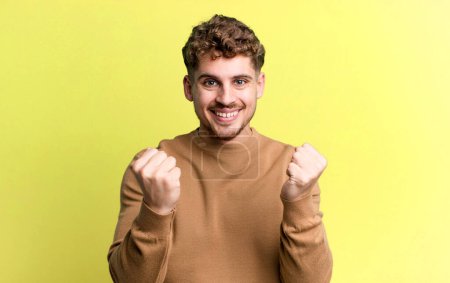 Téléchargez les photos : Young adult caucasian man shouting triumphantly, laughing and feeling happy and excited while celebrating success - en image libre de droit