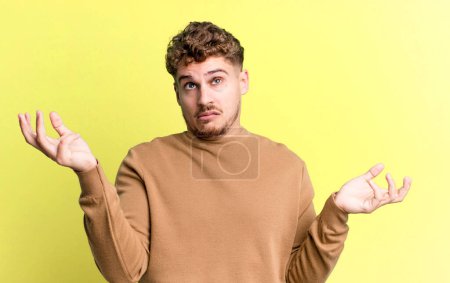 Photo for Young adult caucasian man shrugging with a dumb, crazy, confused, puzzled expression, feeling annoyed and clueless - Royalty Free Image