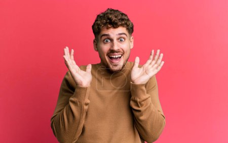 Photo for Young adult caucasian man feeling shocked and excited, laughing, amazed and happy because of an unexpected surprise - Royalty Free Image