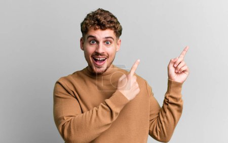 Foto de Young adult caucasian man feeling joyful and surprised, smiling with a shocked expression and pointing to the side - Imagen libre de derechos