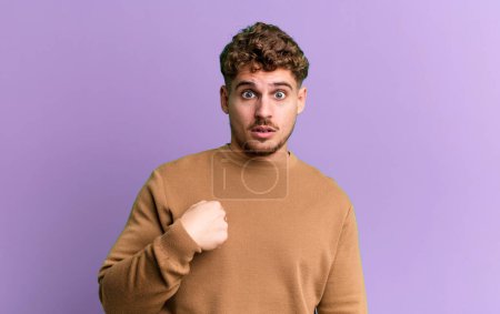 Photo for Young adult caucasian man feeling confused, puzzled and insecure, pointing to self wondering and asking who, me? - Royalty Free Image