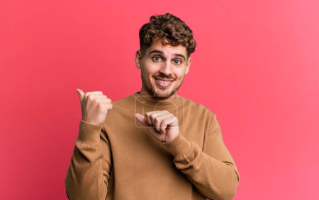 Photo for Young adult caucasian man smiling cheerfully and casually pointing to copy space on the side, feeling happy and satisfied - Royalty Free Image