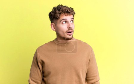 Foto de Young adult caucasian man feeling shocked, happy, amazed and surprised, looking to the side with open mouth - Imagen libre de derechos