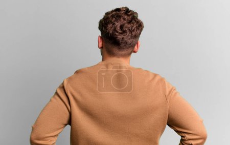 Photo for Young adult caucasian man feeling confused or full or doubts and questions, wondering, with hands on hips, rear view - Royalty Free Image