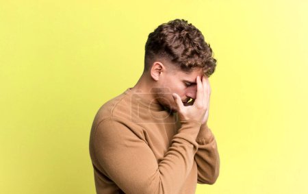 Photo for Young adult caucasian man covering eyes with hands with a sad, frustrated look of despair, crying, side view - Royalty Free Image