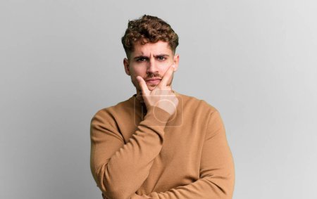 Téléchargez les photos : Young adult caucasian man looking serious, thoughtful and distrustful, with one arm crossed and hand on chin, weighting options - en image libre de droit