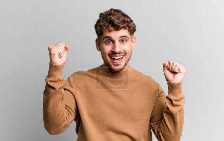 Photo for Young adult caucasian man feeling happy, positive and successful, celebrating victory, achievements or good luck - Royalty Free Image