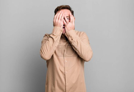 Photo for Covering face with hands, peeking between fingers with surprised expression and looking to the side - Royalty Free Image
