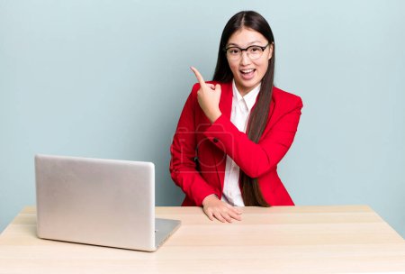Photo for Pretty asian woman looking excited and surprised pointing to the side. business desk concept - Royalty Free Image