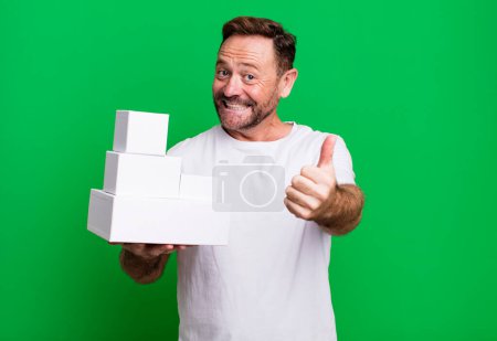 Foto de Hombre de mediana edad sentirse orgulloso, sonriendo positivamente con los pulgares hacia arriba. concepto de paquetes en blanco - Imagen libre de derechos