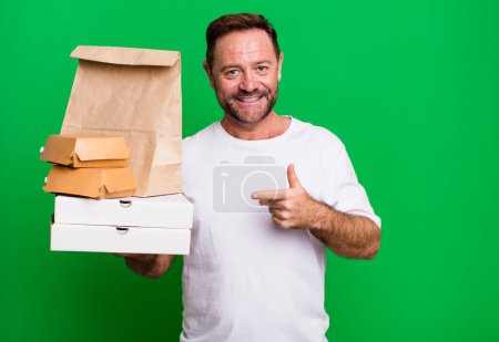 Photo for Middle age man smiling cheerfully, feeling happy and pointing to the side. delivery and fast food take away concept - Royalty Free Image