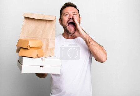 Téléchargez les photos : Homme d'âge moyen se sentant heureux, donnant un grand cri avec les mains à côté de la bouche. livraison et fast food concept à emporter - en image libre de droit