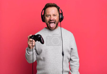 Photo for Middle age man feeling disgusted and irritated and tongue out. gamer concept with a control and headset - Royalty Free Image