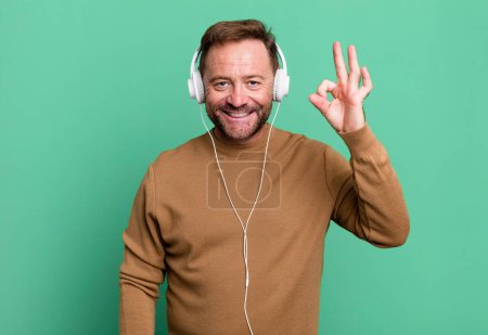 Photo for Middle age man feeling happy, showing approval with okay gesture. listening music with a headphones - Royalty Free Image