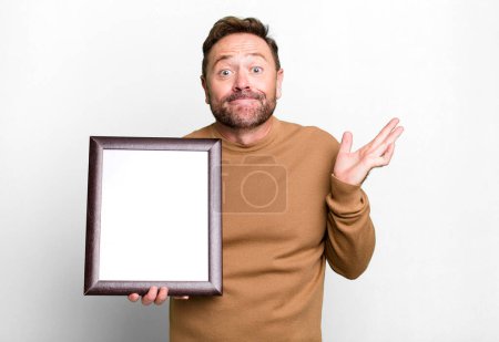 Photo for Middle age man feeling puzzled and confused and doubting with an empty frame - Royalty Free Image