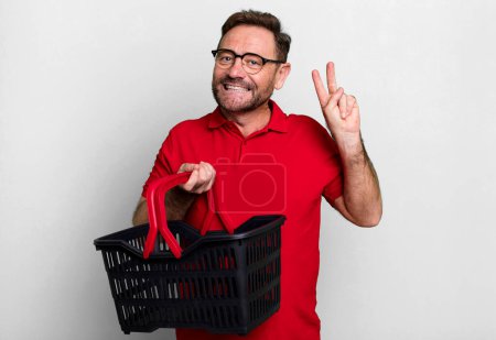 Photo for Middle age man smiling and looking friendly, showing number two. empty shopping basket concept - Royalty Free Image