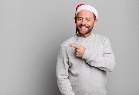 Foto de Hombre de mediana edad sonriendo alegremente, sintiéndose feliz y señalando hacia un lado. concepto de Navidad - Imagen libre de derechos