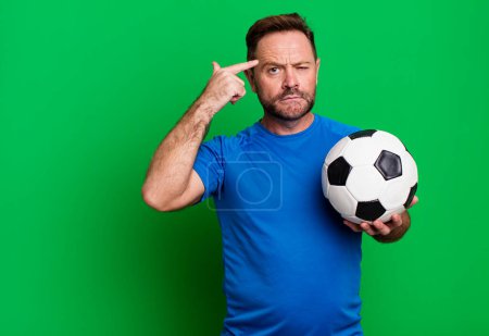 Téléchargez les photos : Homme d'âge moyen se sentant confus et perplexe, montrant que vous êtes fou. avec un ballon de foot. concept de fitness - en image libre de droit