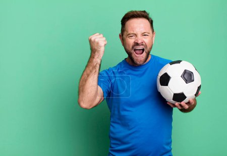 Photo pour Homme d'âge moyen criant agressivement avec une expression en colère. avec un ballon de foot. concept de fitness - image libre de droit