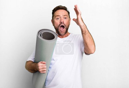 Téléchargez les photos : Homme d'âge moyen criant avec les mains en l'air. avec un tapis de yoga. concept de fitness - en image libre de droit