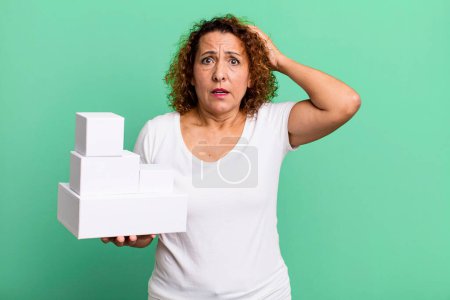 Photo for Pretty middle age woman feeling stressed, anxious or scared, with hands on head. blank white boxes packaging - Royalty Free Image