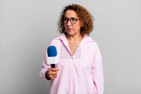 Photo for Pretty middle age woman feeling sad, upset or angry and looking to the side. tv presenter with a microphone concept - Royalty Free Image